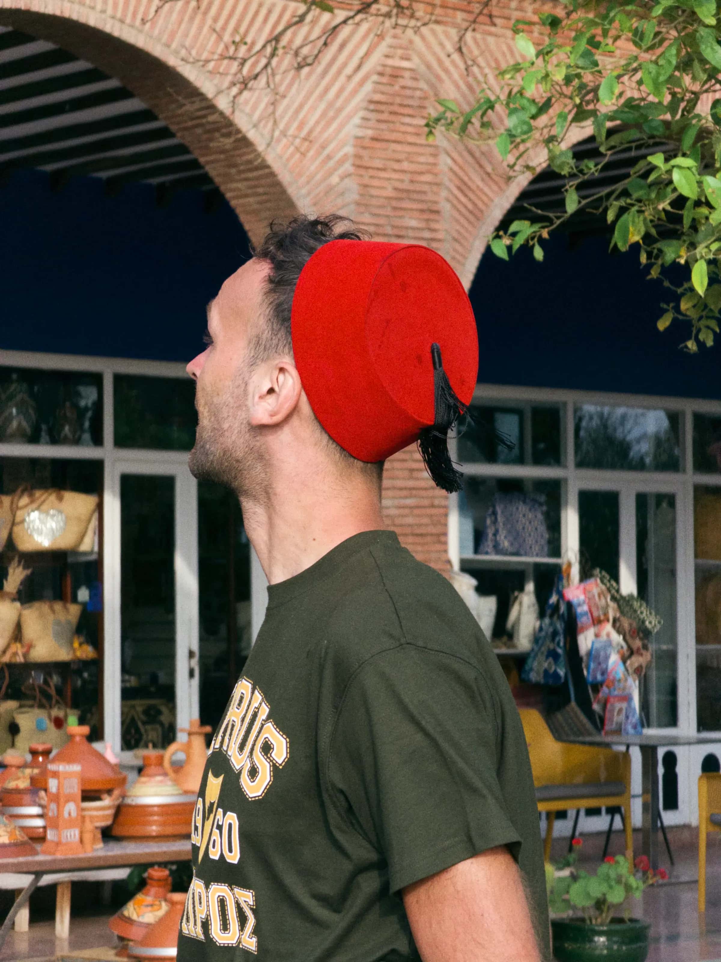 A man in a red fez in a shaded courtyard