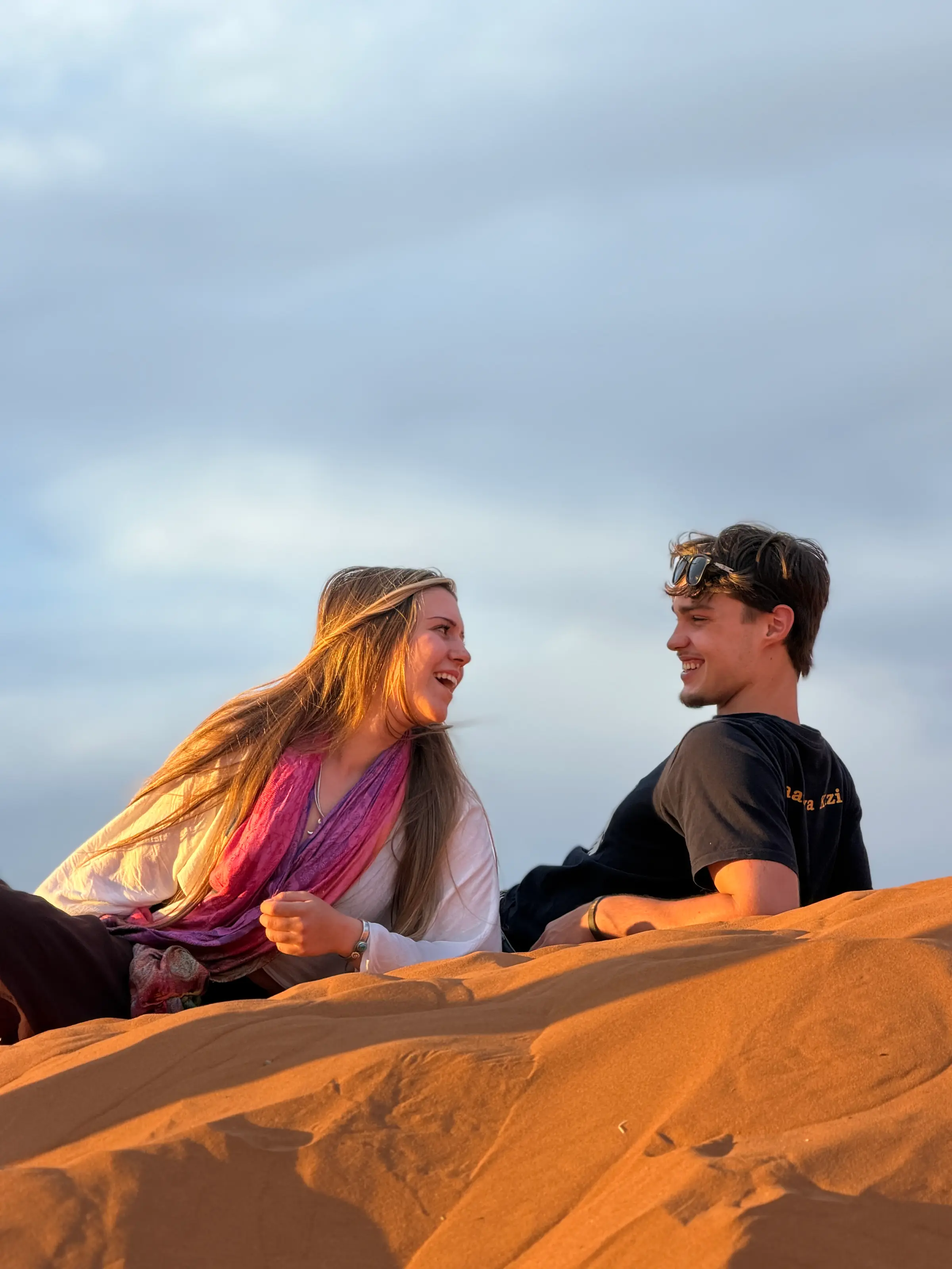 Two travellers laughing on a dune at golden hour