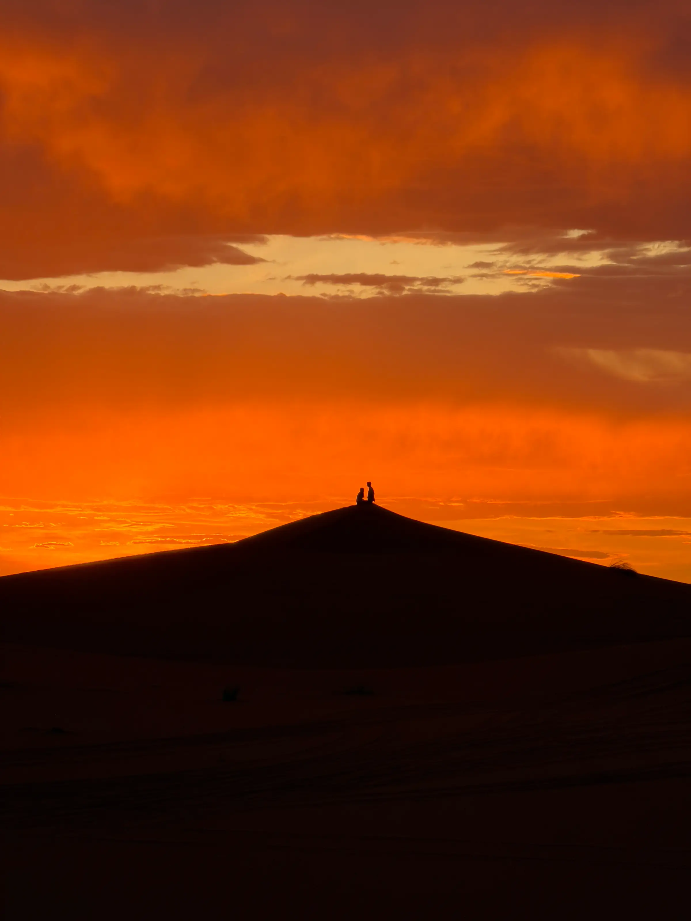 A lone figure on a dune ridge against a burning sunset